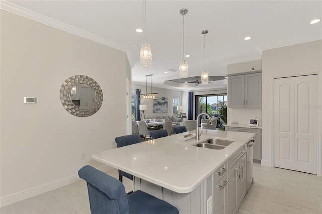 kitchen with sink, light stone counters, an island with sink, pendant lighting, and gray cabinets