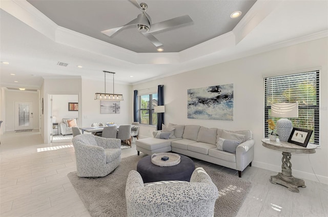 living room with a raised ceiling, ceiling fan, and ornamental molding