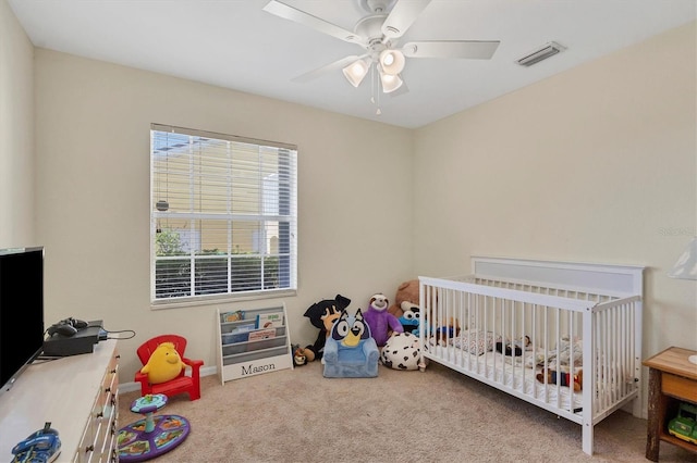 carpeted bedroom featuring ceiling fan and a nursery area