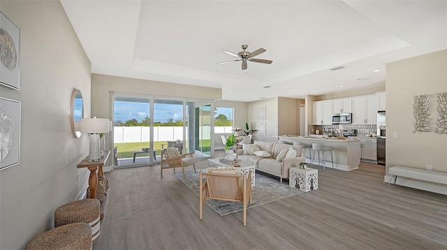 living room with hardwood / wood-style flooring, ceiling fan, and a raised ceiling