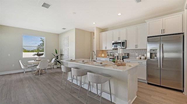 kitchen featuring light hardwood / wood-style floors, white cabinets, an island with sink, and appliances with stainless steel finishes