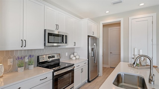 kitchen featuring white cabinetry, sink, stainless steel appliances, light hardwood / wood-style flooring, and backsplash