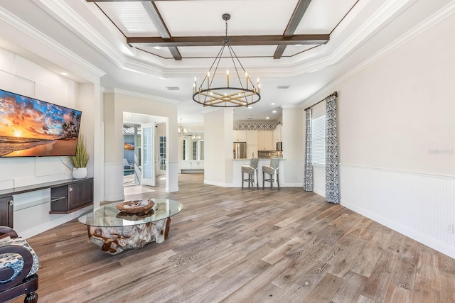 living room with a notable chandelier, wainscoting, light wood-type flooring, beam ceiling, and crown molding