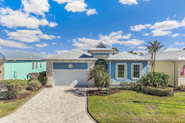 view of front of home featuring metal roof, an attached garage, a standing seam roof, decorative driveway, and a front lawn