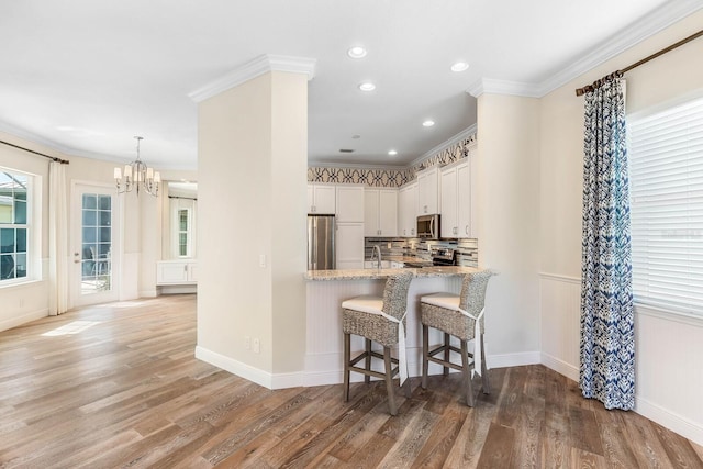 kitchen with a breakfast bar area, ornamental molding, wood finished floors, stainless steel appliances, and backsplash