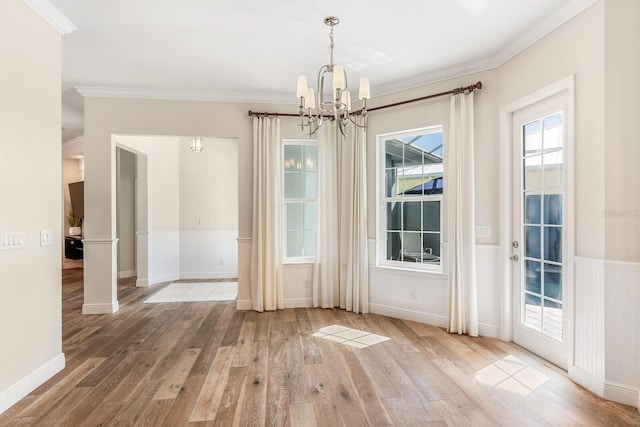 unfurnished dining area with a wainscoted wall, ornamental molding, wood finished floors, and a notable chandelier