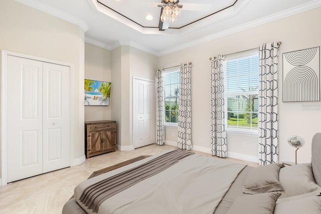 tiled bedroom featuring a raised ceiling, crown molding, baseboards, and two closets