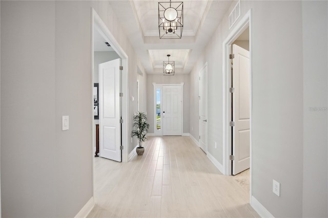 corridor featuring an inviting chandelier, light wood-type flooring, and a tray ceiling