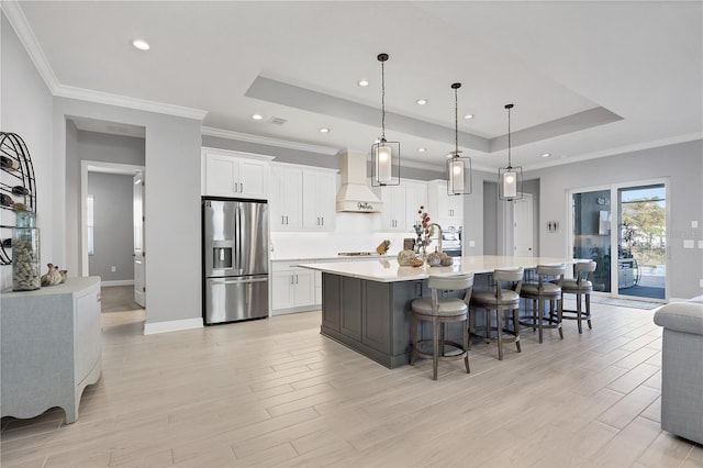 kitchen with hanging light fixtures, stainless steel fridge with ice dispenser, white cabinetry, and custom range hood