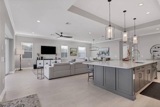 kitchen featuring ceiling fan, sink, a large island with sink, light hardwood / wood-style floors, and hanging light fixtures