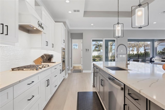 kitchen featuring premium range hood, stainless steel appliances, sink, white cabinets, and hanging light fixtures