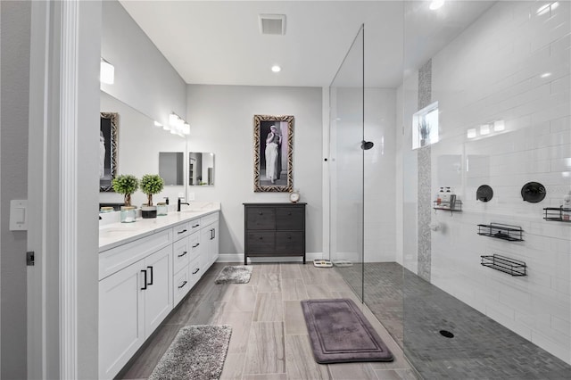 bathroom with hardwood / wood-style floors, vanity, and a tile shower