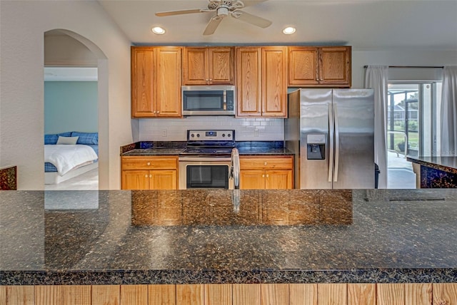 kitchen featuring ceiling fan, decorative backsplash, appliances with stainless steel finishes, and dark stone counters