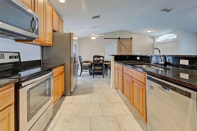 kitchen with dark stone counters, stainless steel appliances, vaulted ceiling, sink, and a barn door