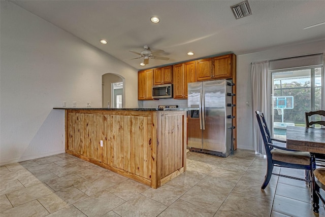 kitchen featuring ceiling fan, kitchen peninsula, appliances with stainless steel finishes, and dark stone counters