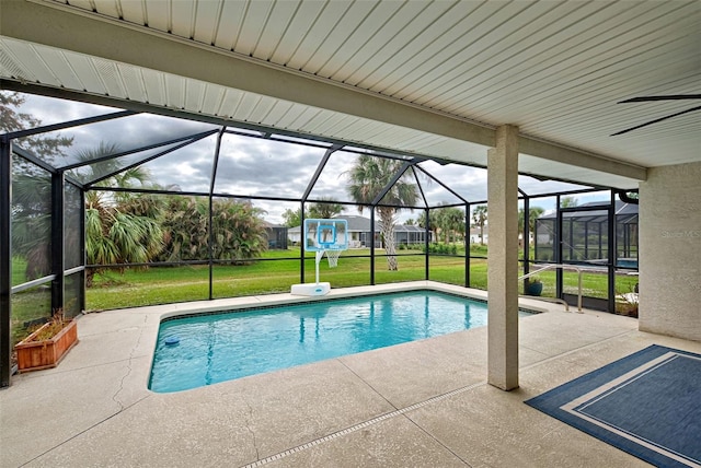 view of swimming pool with glass enclosure, ceiling fan, a patio area, and a yard