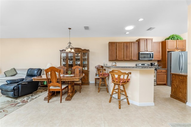 kitchen with a kitchen bar, hanging light fixtures, light tile patterned flooring, and stainless steel appliances