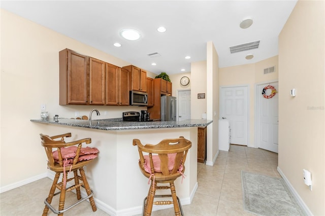 kitchen featuring a kitchen breakfast bar, dark stone countertops, kitchen peninsula, and appliances with stainless steel finishes