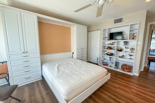 bedroom with a textured ceiling, ceiling fan, dark wood-type flooring, and multiple closets