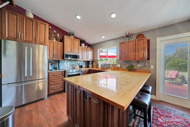 kitchen with kitchen peninsula, a textured ceiling, lofted ceiling, a breakfast bar, and appliances with stainless steel finishes