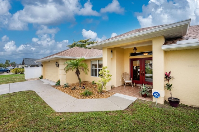 doorway to property with stucco siding, french doors, a yard, a garage, and driveway