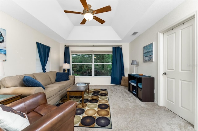 carpeted living room with a raised ceiling, visible vents, and ceiling fan