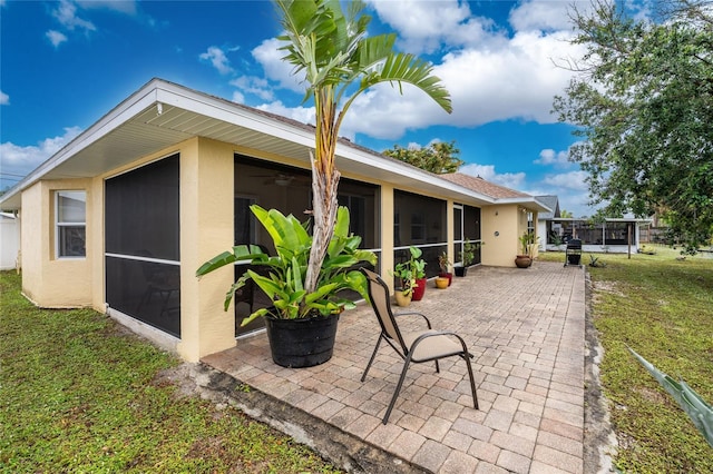 rear view of house featuring stucco siding, a patio, a yard, and a sunroom