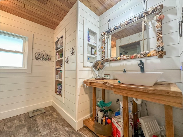 bathroom featuring wood-type flooring, wooden walls, wooden ceiling, and sink