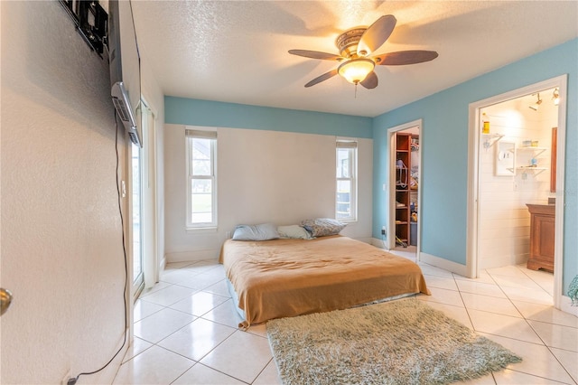 tiled bedroom with a walk in closet, ensuite bathroom, a textured ceiling, ceiling fan, and a closet