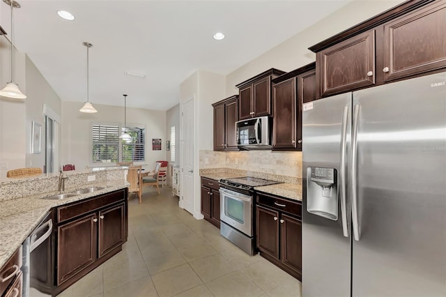 kitchen featuring light stone countertops, backsplash, stainless steel appliances, sink, and decorative light fixtures