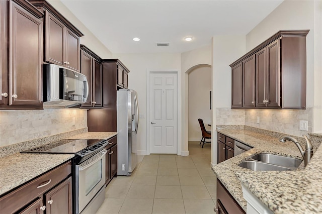 kitchen featuring backsplash, sink, light stone countertops, light tile patterned flooring, and stainless steel appliances