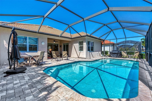 view of pool featuring glass enclosure, ceiling fan, and a patio