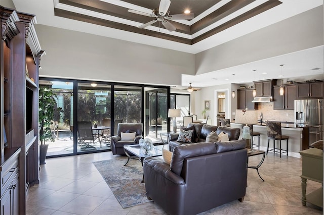 living room featuring a raised ceiling, ceiling fan, crown molding, sink, and a high ceiling