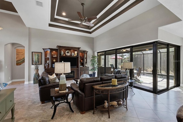 living room featuring a raised ceiling, ceiling fan, a towering ceiling, and ornamental molding