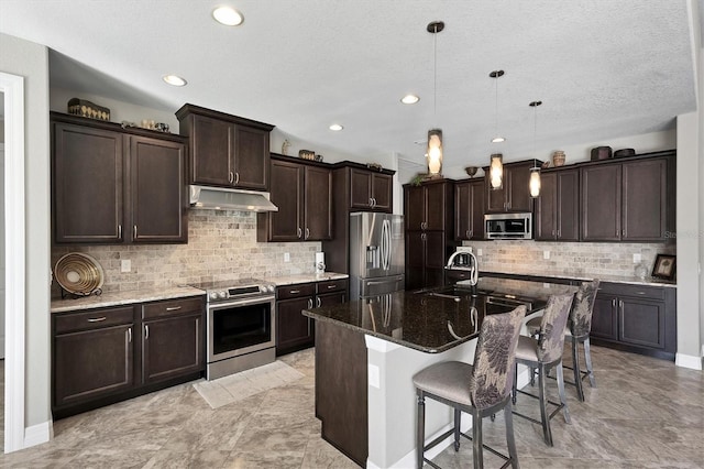 kitchen with a kitchen island with sink, sink, appliances with stainless steel finishes, decorative light fixtures, and a kitchen bar