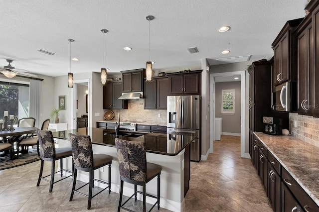 kitchen featuring decorative backsplash, a center island with sink, pendant lighting, and appliances with stainless steel finishes