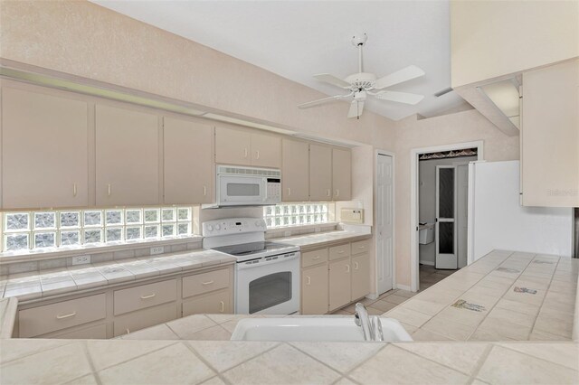 kitchen featuring tile countertops, white appliances, sink, vaulted ceiling, and cream cabinetry