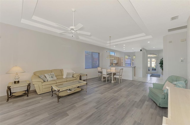 living room featuring light wood-type flooring, ceiling fan, a raised ceiling, and french doors