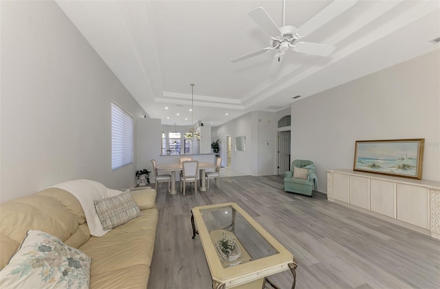 living room with light wood-type flooring, ceiling fan, and a tray ceiling