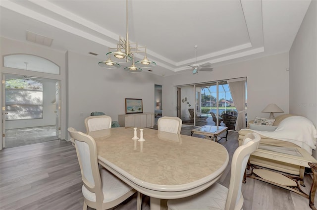 dining space featuring ceiling fan, a tray ceiling, and light hardwood / wood-style flooring