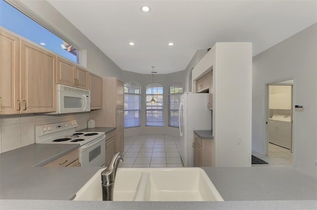 kitchen with white appliances, decorative light fixtures, washing machine and clothes dryer, light brown cabinetry, and sink