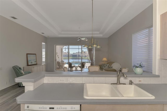 kitchen with pendant lighting, dishwasher, sink, a raised ceiling, and a water view