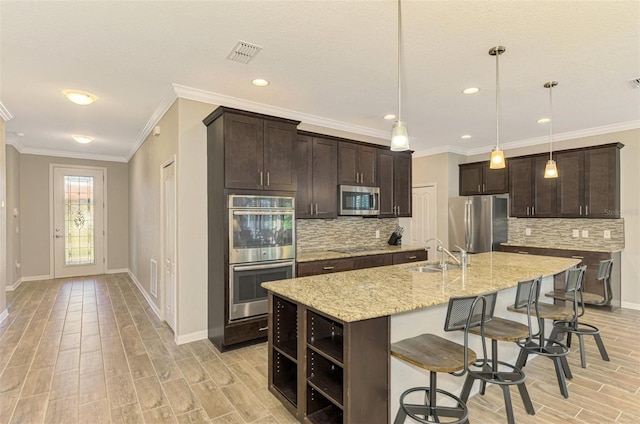 kitchen with a kitchen island with sink, light stone countertops, decorative light fixtures, dark brown cabinetry, and stainless steel appliances