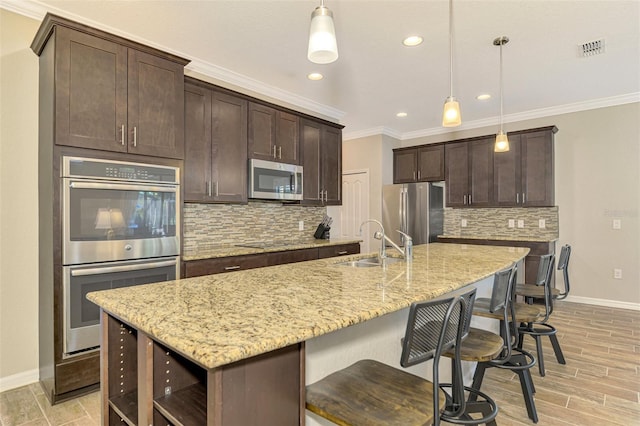 kitchen featuring appliances with stainless steel finishes, backsplash, decorative light fixtures, and a center island with sink