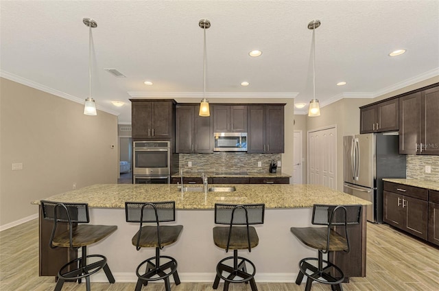 kitchen featuring stainless steel appliances, hanging light fixtures, and a kitchen island with sink