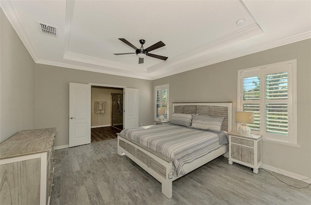 bedroom with a tray ceiling, multiple windows, ceiling fan, and hardwood / wood-style flooring