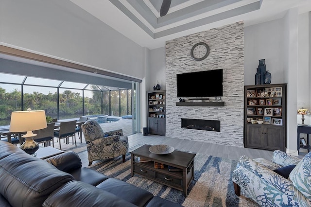 living room featuring a tray ceiling, a stone fireplace, a towering ceiling, and hardwood / wood-style flooring