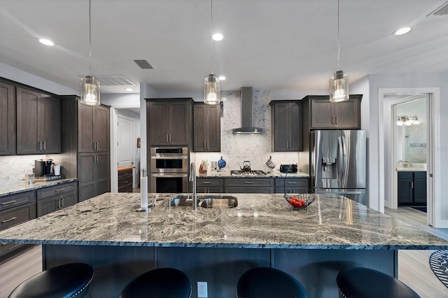 kitchen with appliances with stainless steel finishes, decorative light fixtures, and wall chimney range hood