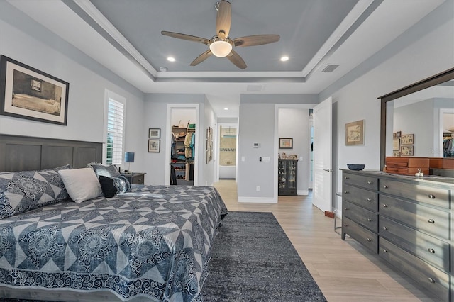 bedroom with ceiling fan, a spacious closet, a tray ceiling, and a closet