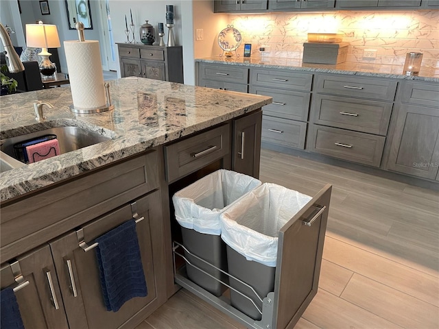 kitchen featuring sink, light hardwood / wood-style floors, light stone counters, and backsplash